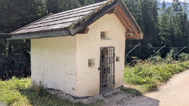 Petite chapelle blanche au bord d’un chemin de montagne.