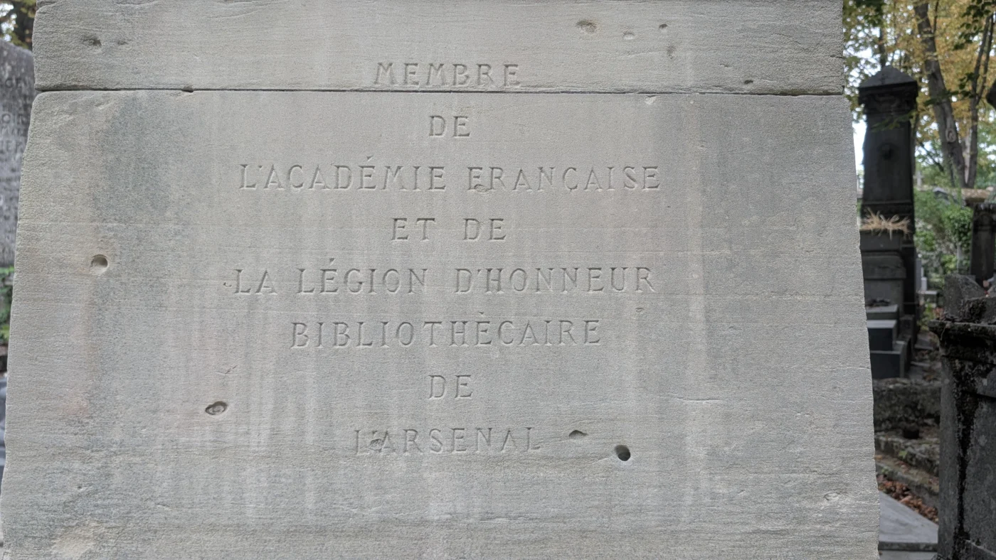 Cavités visibles dans la pierre de la tombe de Charles Nodier autour de l’inscription rappelant qu’il fut membre de l’Académie française et bibliothécaire de l’Arsenal.
